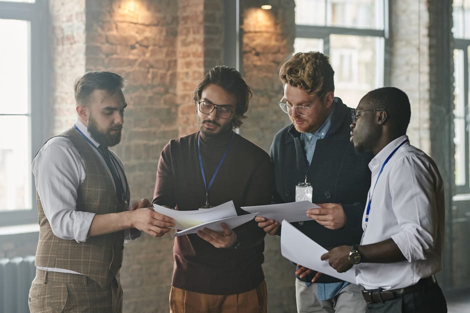 A diverse group of business professionals reviewing documents during a meeting in an industrial-style office space.