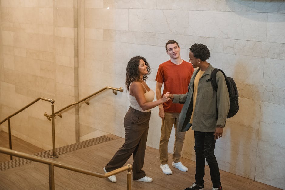 Positive diverse friends in casual clothes talking and greeting while standing in light hallway with stairs